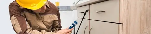 Roach exterminator applying treatment under kitchen cabinets in Clearwater, FL