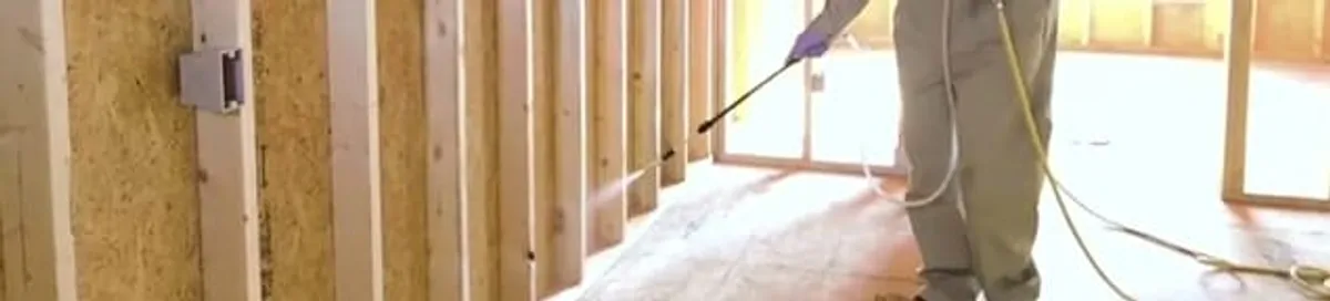 Termite treatment technician applying spray along framing and unfinished walls in Clearwater, FL