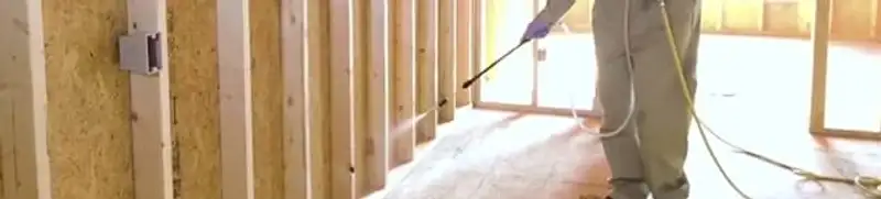 Termite treatment technician applying spray along framing and unfinished walls in Clearwater, FL
